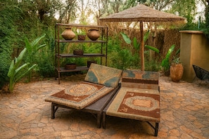 Een rustieke buitenruimte met een geweven parasol, een metalen plank met keramiek en een terras met stenen tegels.