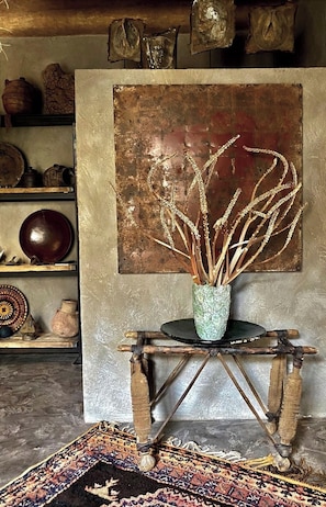 Een rustiek interieur met een houten tafel, een vaas met gedroogde planten en een wanddecoratie met een structuur.