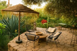 Eine Terrasse im Freien mit Steinboden, einem Reetdachschirm und modernen Korbstühlen.