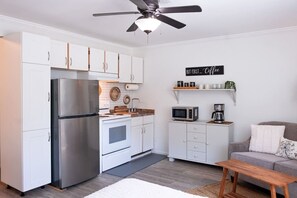 A compact kitchen with white cabinets, a stainless steel refrigerator, a microwave, and a coffee machine.