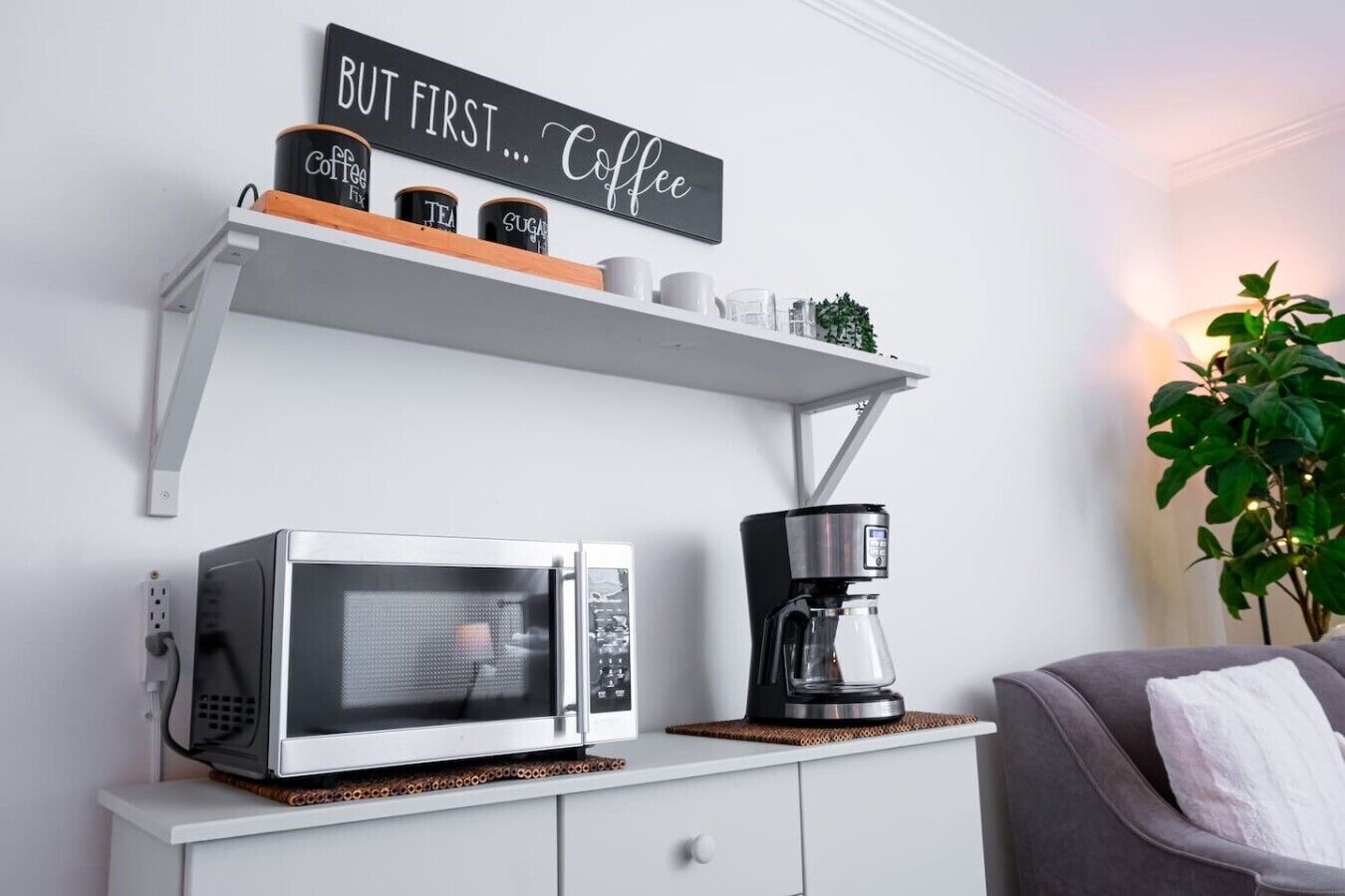 A kitchen area with a microwave, coffee maker, and a shelf with coffee-related items.