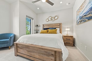 A bedroom with a wooden bed, a nightstand, a blue chair, and a ceiling fan. - LoHi 5BR | Rooftop Fire Pit | Theater | Gym (Denver)