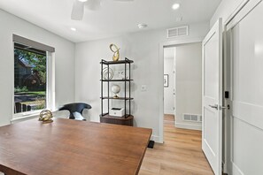 A modern room with a wooden table, a black chair, a decorative metal shelf with a globe and a white sculpture, and a window with a view of a house and greenery. - LoHi 5BR | Rooftop Fire Pit | Theater | Gym (Denver)