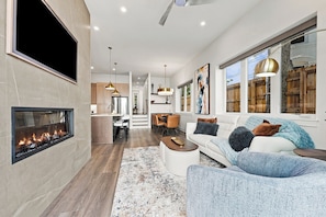 A modern living room with a fireplace, a dining area, and a kitchen.