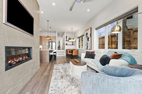 A modern living room with a fireplace, a dining area, and a kitchen.