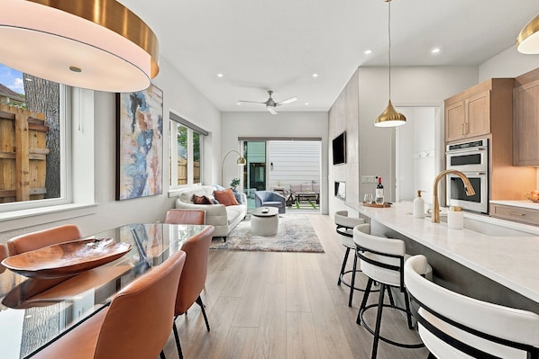 A modern kitchen with a central island, bar seating, and a dining area with leather chairs.
