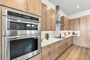 A modern kitchen with stainless steel appliances, wooden cabinets, and a marble countertop. - LoHi 5BR | Rooftop Fire Pit | Theater | Gym (Denver)