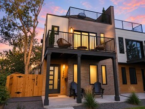 A modern two-story house with a balcony, a wooden fence, and outdoor seating.