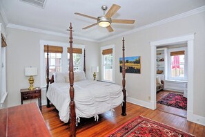 Ein Bett mit Baldachin, Deckenventilator, Holzboden und ein roher Teppich.