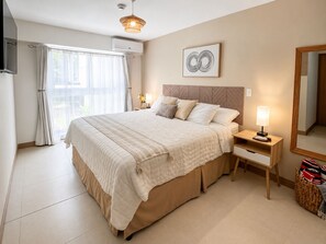 Ein Schlafzimmer mit einem großen Bett, Nachttischen, einer Lampe, einem Spiegel und einem Fenster mit Vorhängen.
