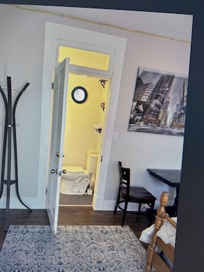 Quarto com porta amarela, uma cadeira, uma mesa pequena e um quadro na parede.