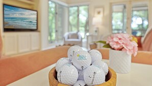 Ein Zimmer mit Fernseher, der eine Strandansicht zeigt, einer Schüssel mit Golfbällen und einer Blumenvase.