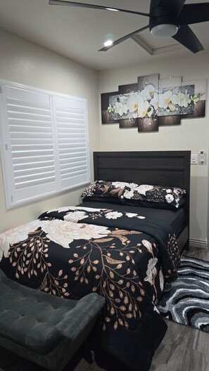 A bedroom with a bed, a bench, a ceiling fan, a wall-mounted artwork, and a window with blinds.
