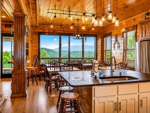 Un intérieur en bois avec un îlot de cuisine, des sièges de bar et de grandes fenêtres offrant une vue sur les montagnes.