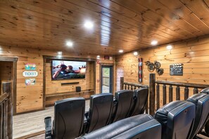 Cabin theater room with large TV, reclining seating, and rustic wood interiors ideal for family movie nights and entertainment. - Smoky Mountain 13BR Lodge | Pool & Hot Tub | Sleeps 58 (Sevierville)