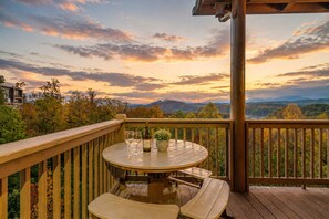 A wooden deck with a round table and chairs, overlooking a mountainous landscape during sunset. - Smoky Mountain 13BR Lodge | Pool & Hot Tub | Sleeps 58 (Sevierville)