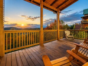 Une terrasse en bois offrant une vue sur les montagnes au coucher du soleil.