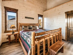 A cozy bedroom with a wooden bed, a bench, a nightstand, and a wall sign. - Luxury Smoky Mountain Cabin w/ Indoor Pool, Theater & Panoramic Views (Sevierville)