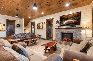 A cozy living room with a stone fireplace, wooden ceiling, and a large painting of a landscape. - Luxury Smoky Mountain Cabin w/ Indoor Pool, Theater & Panoramic Views (Sevierville)