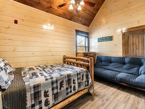A wooden cabin room with a bed, a blue sofa, and a wooden ceiling.