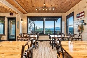 A wooden interior with a large table and chairs, a view through the windows, and a flag on the wall. - Luxury Smoky Mountain Cabin w/ Indoor Pool, Theater & Panoramic Views (Sevierville)