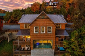 A two-story log cabin with a balcony, a pool, and a view of autumn trees.