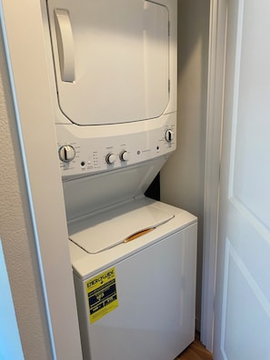Een compact, wit was- en droogcombitoestel, gemonteerd aan de muur, met bedieningsknoppen en een geel energielabel.