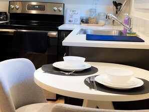Een moderne keuken met een fornuis, spoelbak en een eethoek met borden en bestek.
