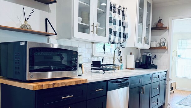 A modern kitchen with black cabinets, a stainless steel microwave, and a dishwasher. - Home near DFW Airport & Arlington World Cup. Perfect for groups and families. (Irving)