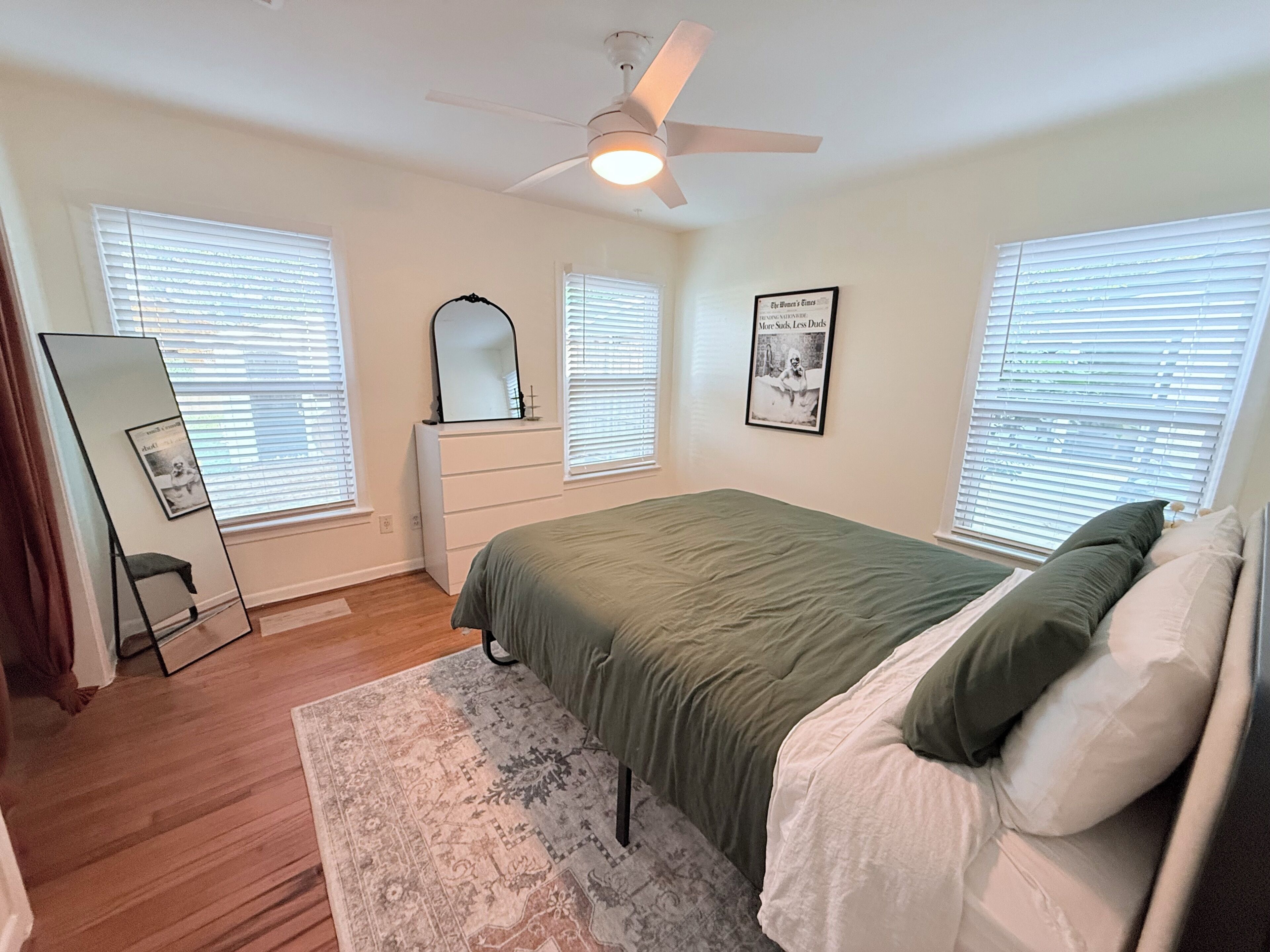 A bedroom with a bed, dresser, mirror, and ceiling fan.