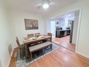A dining area with a wooden table, chairs, and a bench, leading to a kitchen with modern appliances. - Home near DFW Airport & Arlington World Cup. Perfect for groups and families. (Irving)