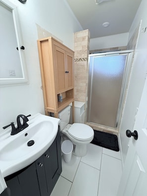 Ein Badezimmer mit weißem Waschbecken, Holzschrank, Toilette und einer Duschkabine aus Glas.