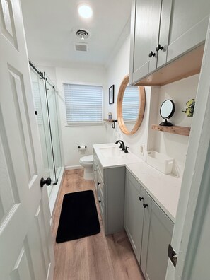 A bathroom with a shower, toilet, sink, and mirror. - Home near DFW Airport & Arlington World Cup. Perfect for groups and families. (Irving)
