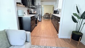 A modern kitchen with dark cabinets, a refrigerator, and a dining area with a table and chairs. - Home near DFW Airport & Arlington World Cup. Perfect for groups and families. (Irving)
