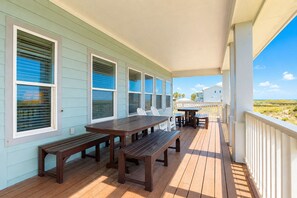 Eine überdachte Terrasse im Freien mit Holzbanken und einem Tisch, mit Blick auf einen Strand.