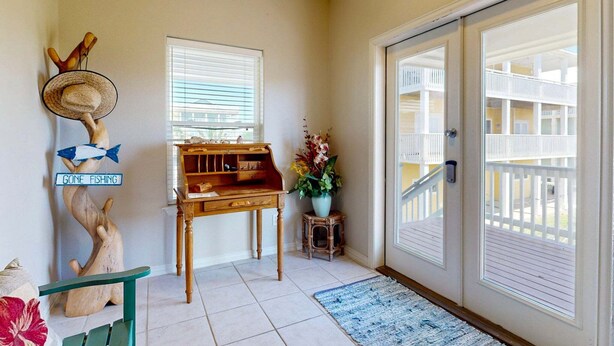 A room with a wooden desk, a small stool, a decorative fish sculpture, a sign saying 'GONE FISHING', a window with blinds, a potted plant, and a sliding glass door leading to a balcony. - MR288 Shared Pools, Golf Cart Included, Pet Friendly (Port Aransas)