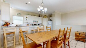 A kitchen with a wooden dining table and chairs, white cabinets, and a hanging light fixture. - MR288 Shared Pools, Golf Cart Included, Pet Friendly (Port Aransas)