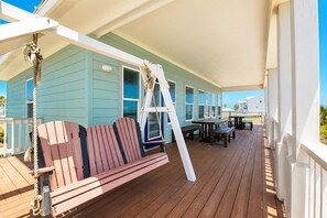 A wooden deck with a swing, a table, and chairs. - MR288 Shared Pools, Golf Cart Included, Pet Friendly (Port Aransas)