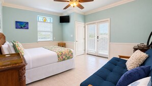 A bedroom with a bed, a blue sofa, a wooden side table, a ceiling fan, and a window with blinds. - MR288 Shared Pools, Golf Cart Included, Pet Friendly (Port Aransas)