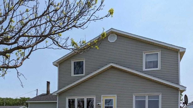 Une maison à deux étages avec un porche à l’avant, une petite terrasse et une antenne parabolique bien visible.