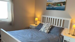 Une chambre à coucher avec un lit, des tables de chevet, une lampe, un tableau et une fenêtre avec des rideaux.