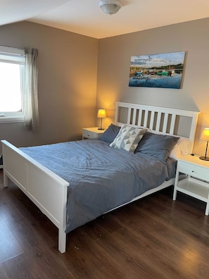 A bedroom with a bed, nightstands, a lamp, a painting, and a window with curtains.