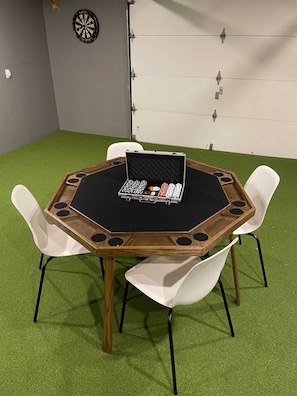 Een ronde tafel met een zwart oppervlak en houten frame, omringd door witte stoelen, geplaatst op kunstgras.