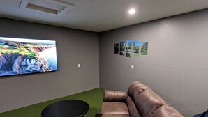 Une pièce avec un canapé en cuir marron, une petite table noire et un grand téléviseur à écran plat fixé au mur.