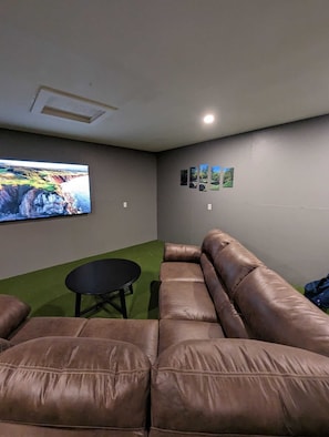 Een kamer met een bruine leren bank, een klein zwart tafeltje en een grote flatscreen-tv aan de muur.