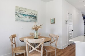 Een eetgedeelte met een ronde tafel, vier houten stoelen, een vaas met gedroogde planten, een schilderij aan de muur en een deur met een lamp.