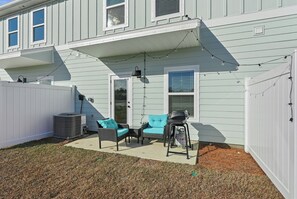 En overdækket terrasse med udendørs møbler, grill og lyskæder.