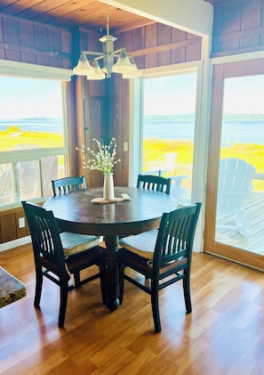A round wooden table with chairs, a vase with flowers, and a view of the outdoors through large windows. - Waltz Seaside Home (Vashon)