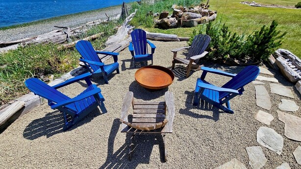 Une terrasse avec quatre chaises Adirondack bleues, une table en bois et un foyer extérieur.