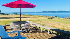 Une terrasse dotée de mobilier d’extérieur, d’un parasol rouge et offrant une vue sur l’eau.